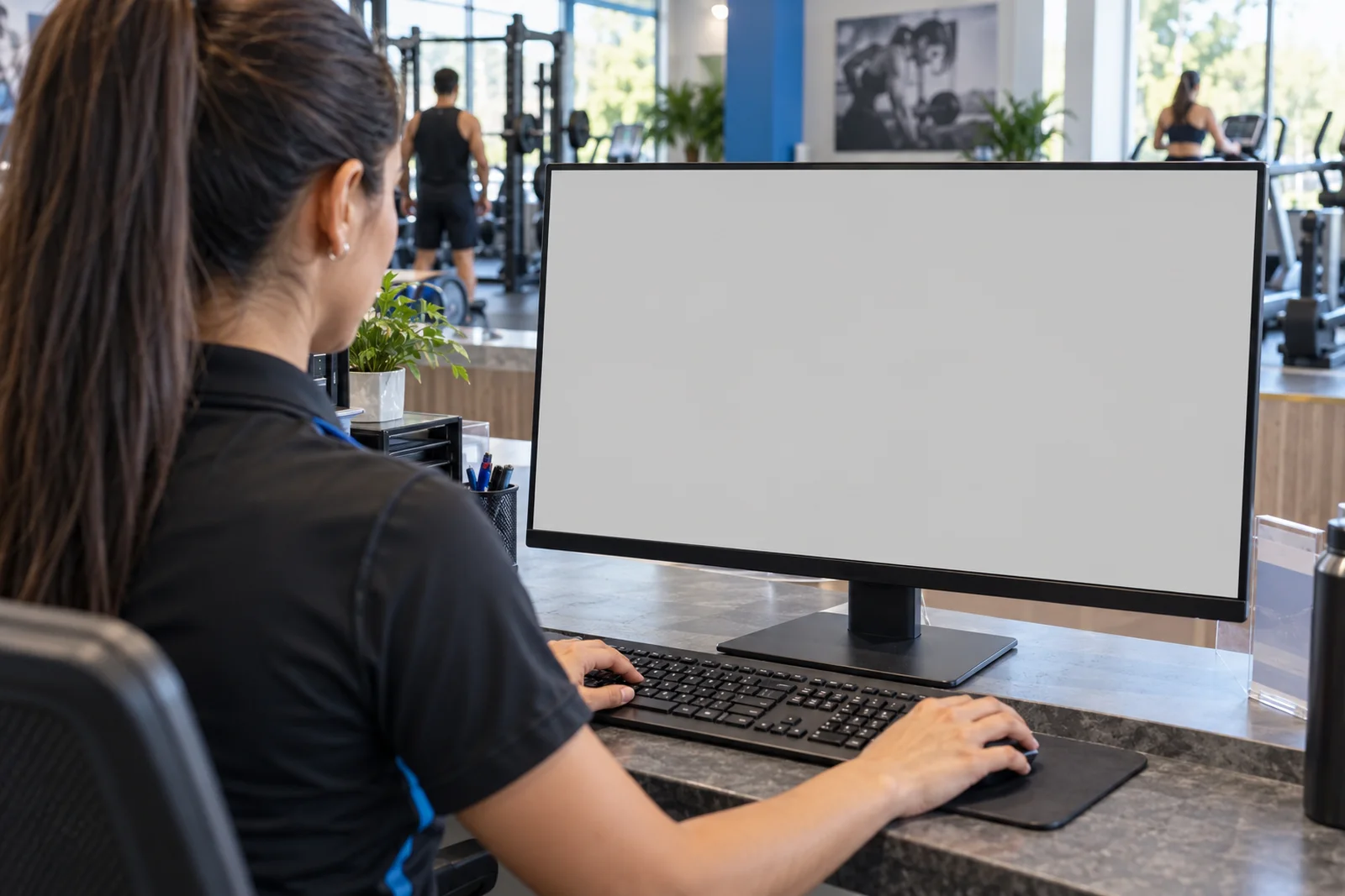 Recepcionista trabajando frente al monitor en un gimnasio. Pantalla: Ficha del cliente.
